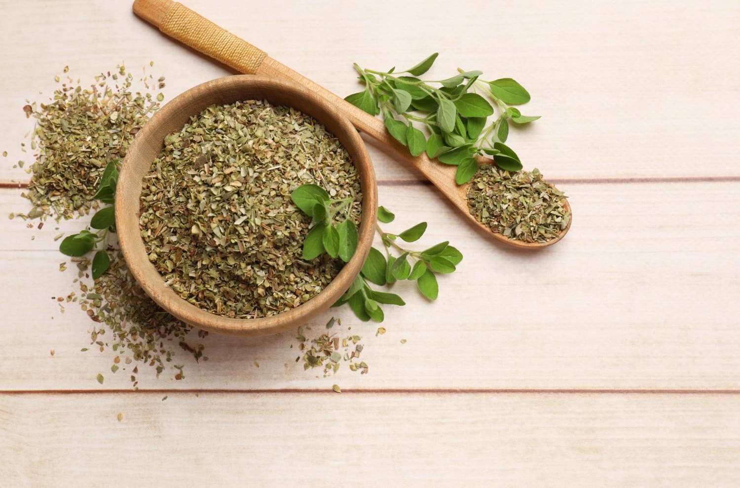 Oregano seco en una cuchara y hojas verdes en una mesa de madera